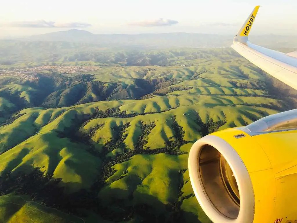 A Frontier Airlines plane viewed from an airplane window, showcasing the airline's green tail and logo, emphasizing the budget carrier aesthetic and functional design of the aircraft's interior.