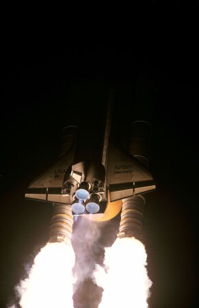 Night launch of the Space Shuttle Discovery highlighting the powerful engines needed to overcome Earth's gravity, demonstrating the concept of weight and mass in rocket propulsion.