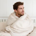 man wrapped in bed sheet on white bed