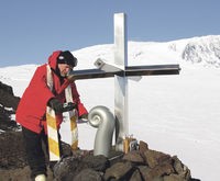 The priest sprinkling sacred water from Aoraki/Mount Cook around the foot of the memorial cross during the Mount Erebus memorial service.