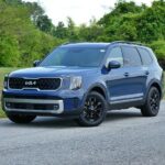 Front ¾ view of a dark gray 2023 Kia Telluride driving on a paved road