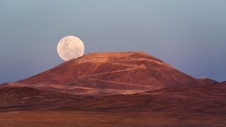 A large moon appearing on the horizon, contrasted with terrestrial objects like mountains, illustrating the moon illusion.