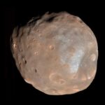 Phobos moon of Mars, captured by NASA's HiRISE camera, showcasing its cratered surface and deep grooves, emphasizing the geological features of Mars's larger moon.