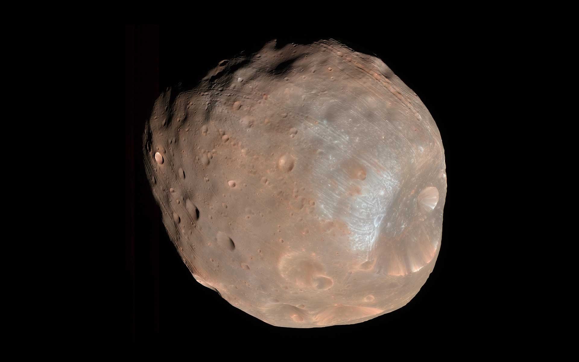 Phobos moon of Mars, captured by NASA's HiRISE camera, showcasing its cratered surface and deep grooves, emphasizing the geological features of Mars's larger moon.