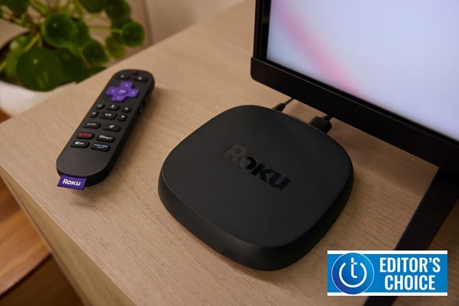 Roku Ultra 2024 on a wooden table with its remote control and a television in the background.