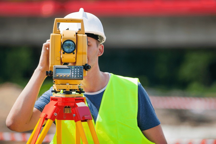 Land Surveyor using equipment to measure land size, ensuring accurate property boundaries. alt=A surveyor uses specialized equipment to precisely measure the dimensions and boundaries of a plot of land. Keywords: land measurement, surveyor, property boundaries, precision tools, real estate survey