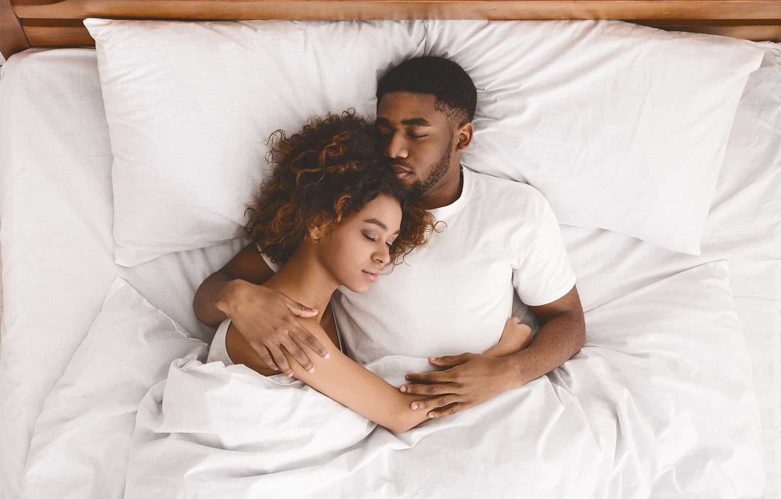 A couple cuddling in a california king bed with white sheets and pillows.