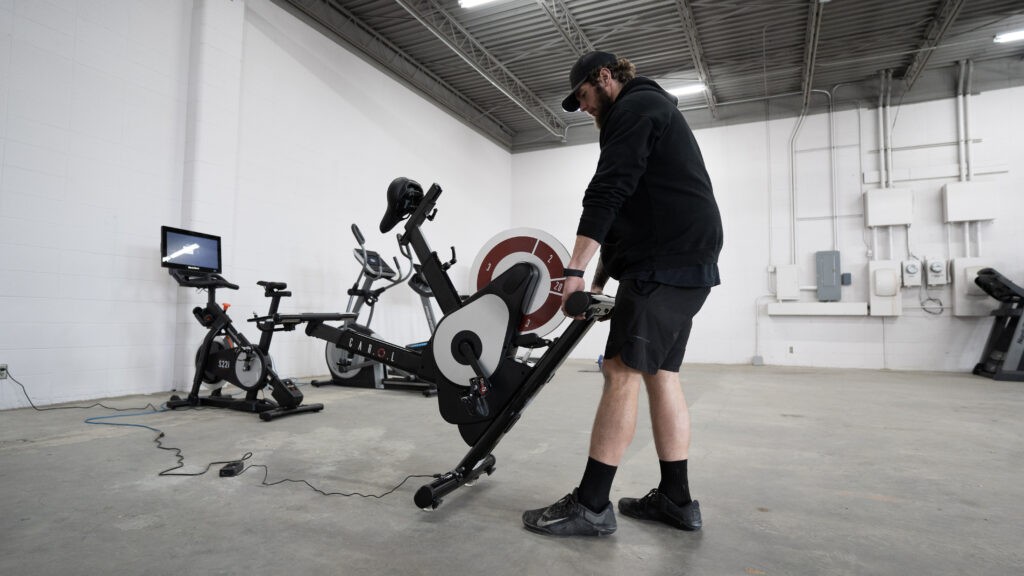 Man moving the CAROL bike, a Peloton alternative.