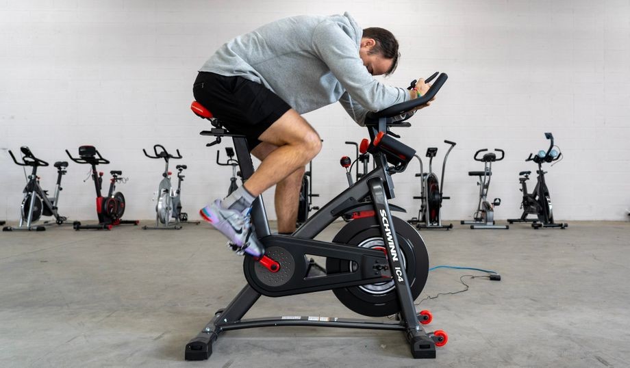 Coop riding the Schwinn IC4 Bike, a Peloton alternative, in a gym with a row of other exercise bikes in background