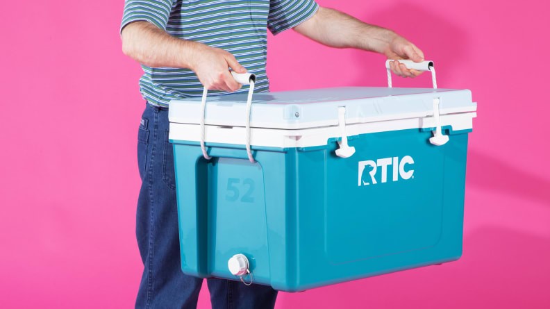 Man holding an RTIC cooler in front of a pink background, highlighting its portability