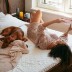 Woman laying in bed reading next to her dog.