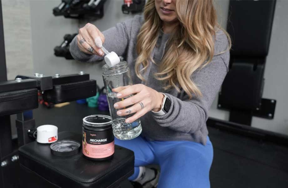 Woman pouring Legion Recharge powder into a water bottle, showcasing the product's ease of use