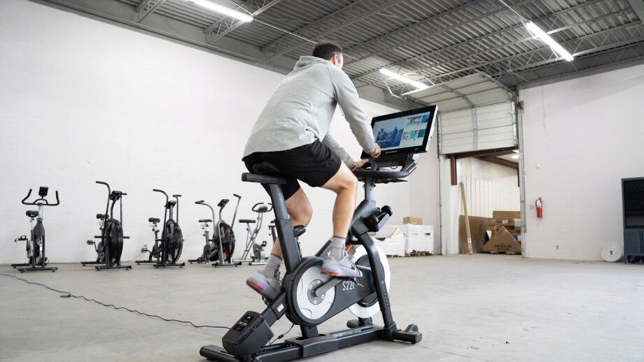 Coop riding a peloton alternative, the NordicTrack S22i studio bike in a home gym with row of other bikes in the background